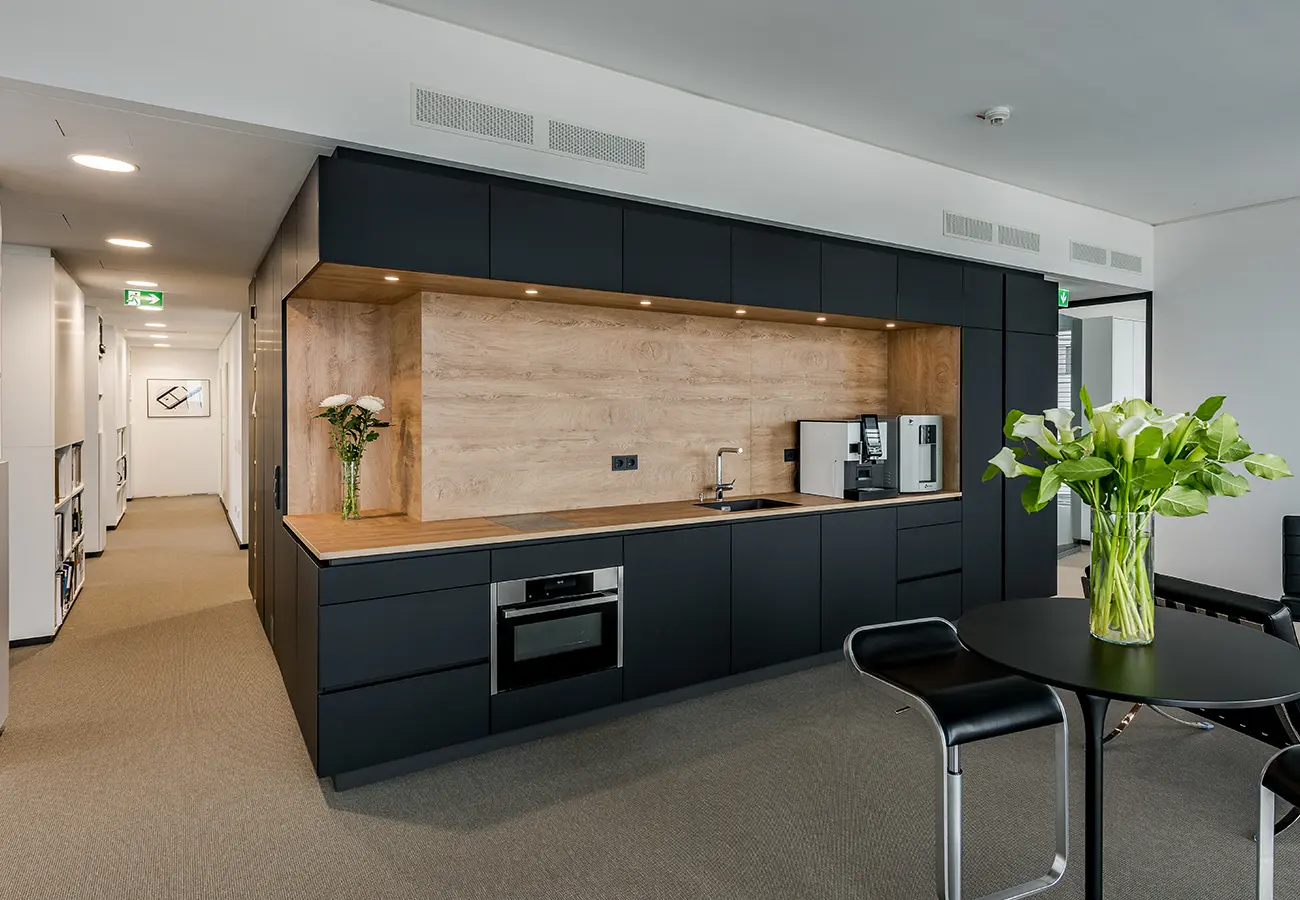 Teeküche im Büro mit dunklen Fronten und Rückwand aus Holz