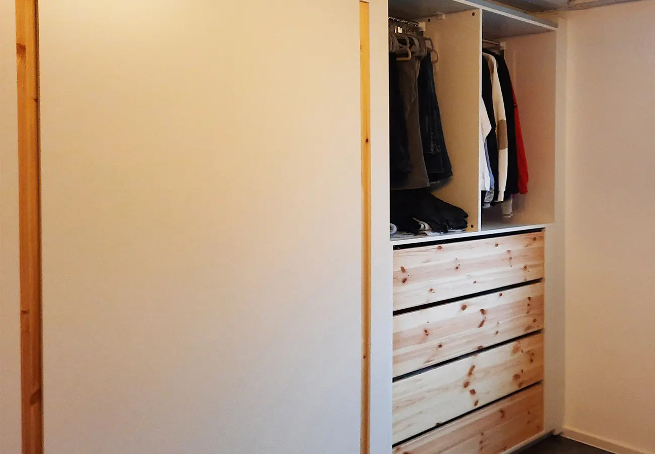 Blick in den offenen Schrank mit Kleiderstange und Holzauszügen