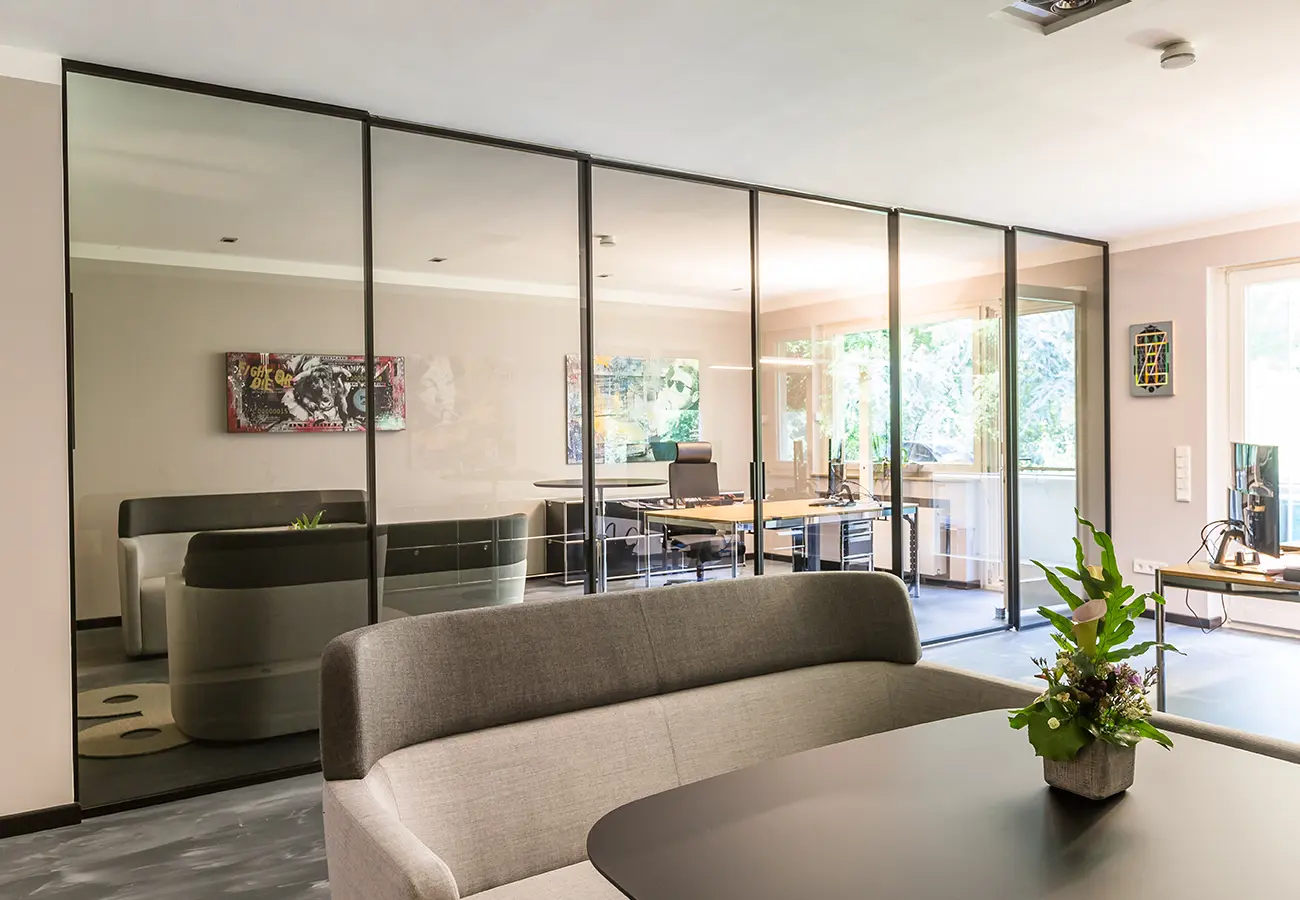 Büro hinter einer raumhohen Schiebetüranlage aus Glas mit Loungebereich
